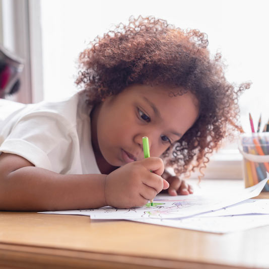 young black girl with curly hair colouring in with a green pencil