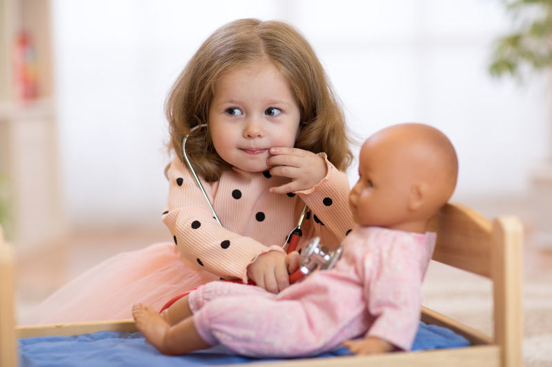 small cute girl playing doctors with a toy baby